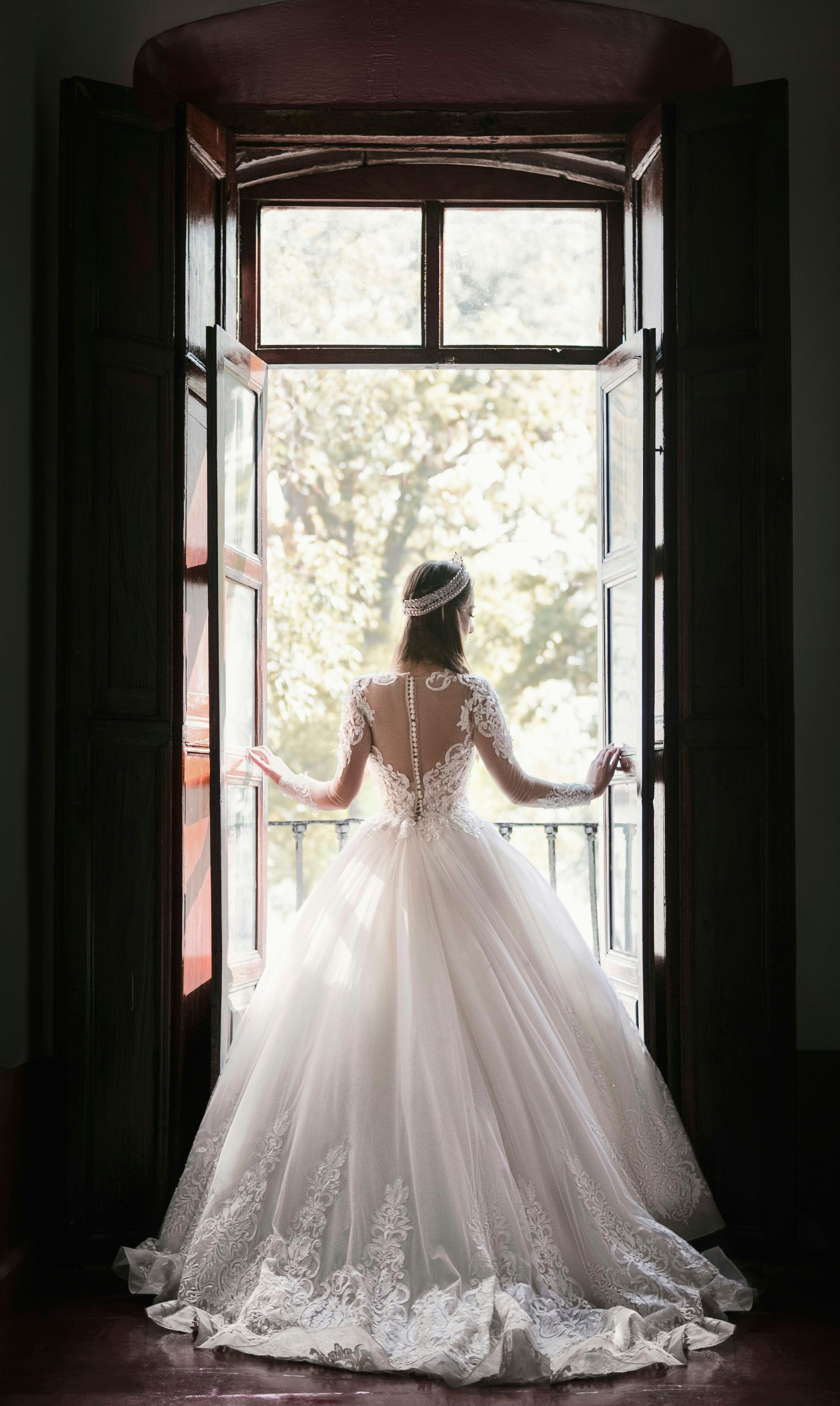 Braut im Spitzenkleid von hinten an einer geöffneten Flügeltür, Tageslicht fällt herein