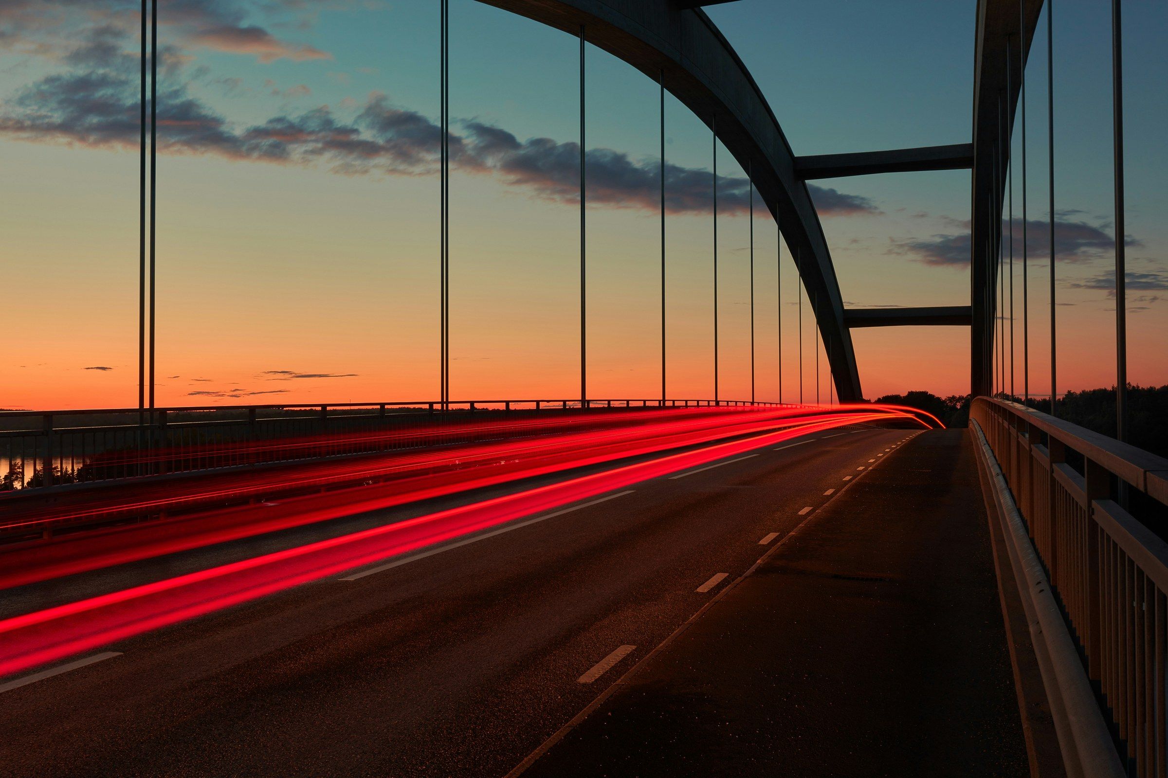 Rote Lichtspuren von Rücklichtern auf einer Brücke im Abendrot