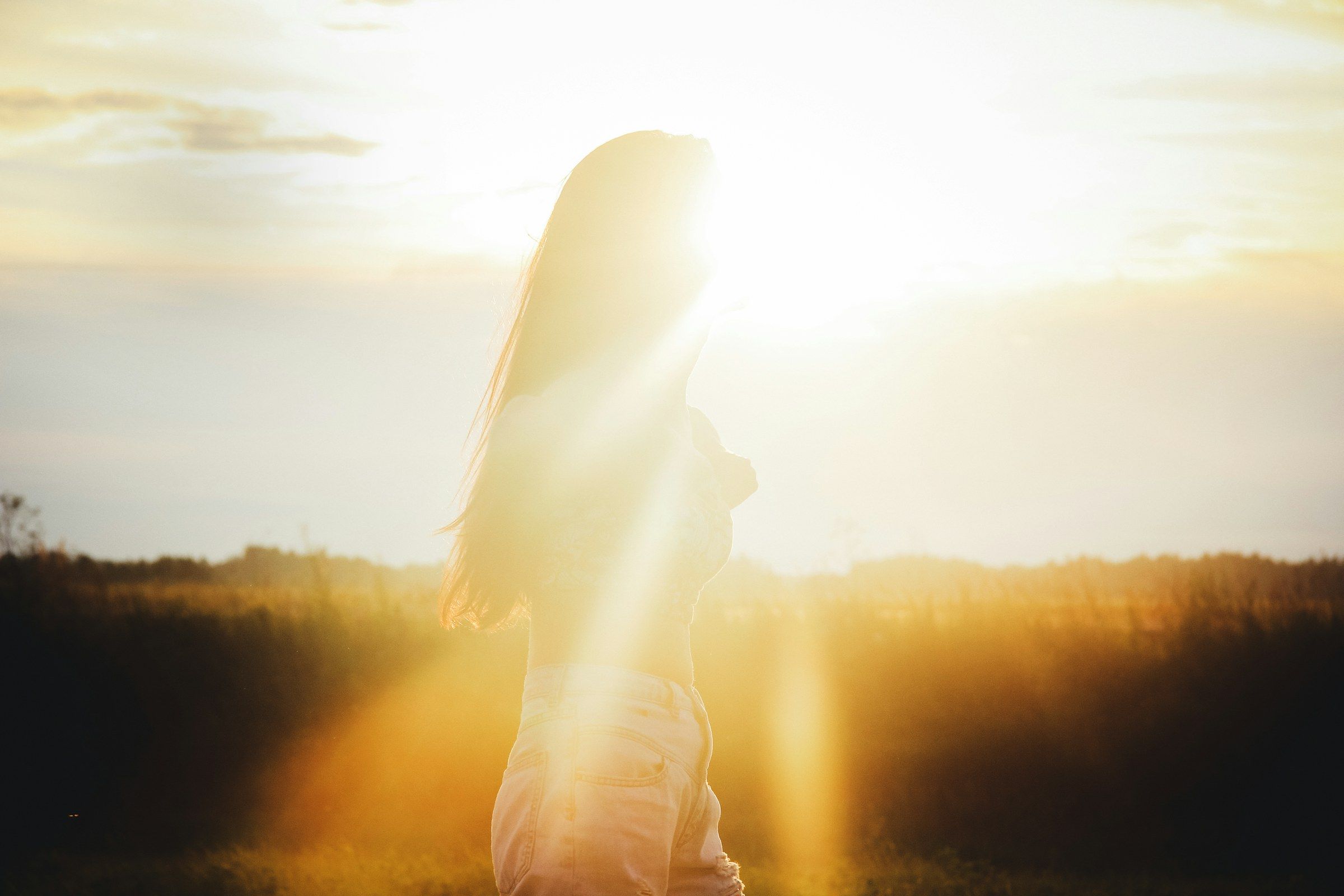 Frau auf einem Feld, die Sonne steht direkt hinter ihr und überstrahlt Haare und Umriss