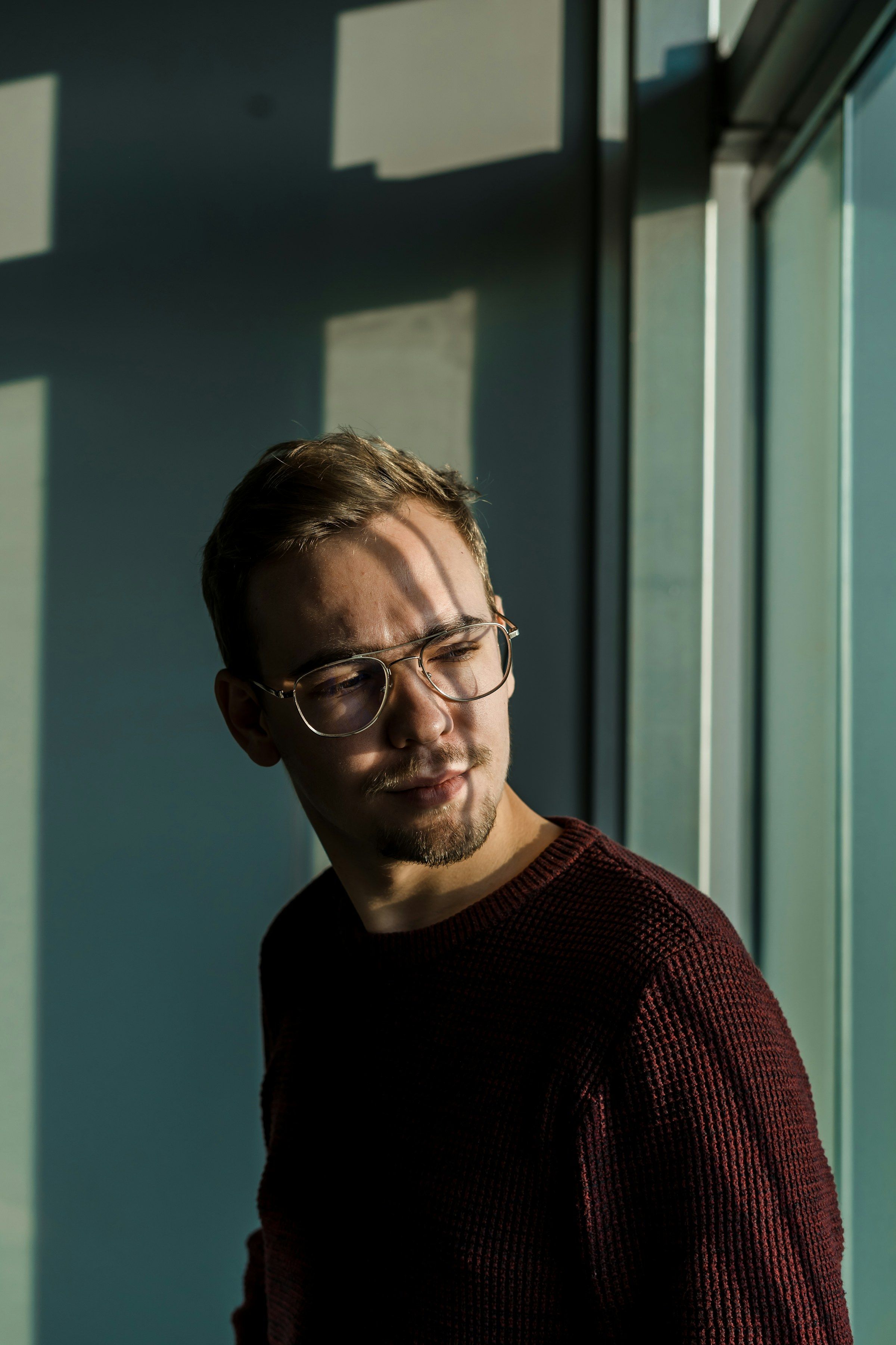 Porträt eines Mannes mit Brille am Fenster, seitliches Tageslicht modelliert das Gesicht
