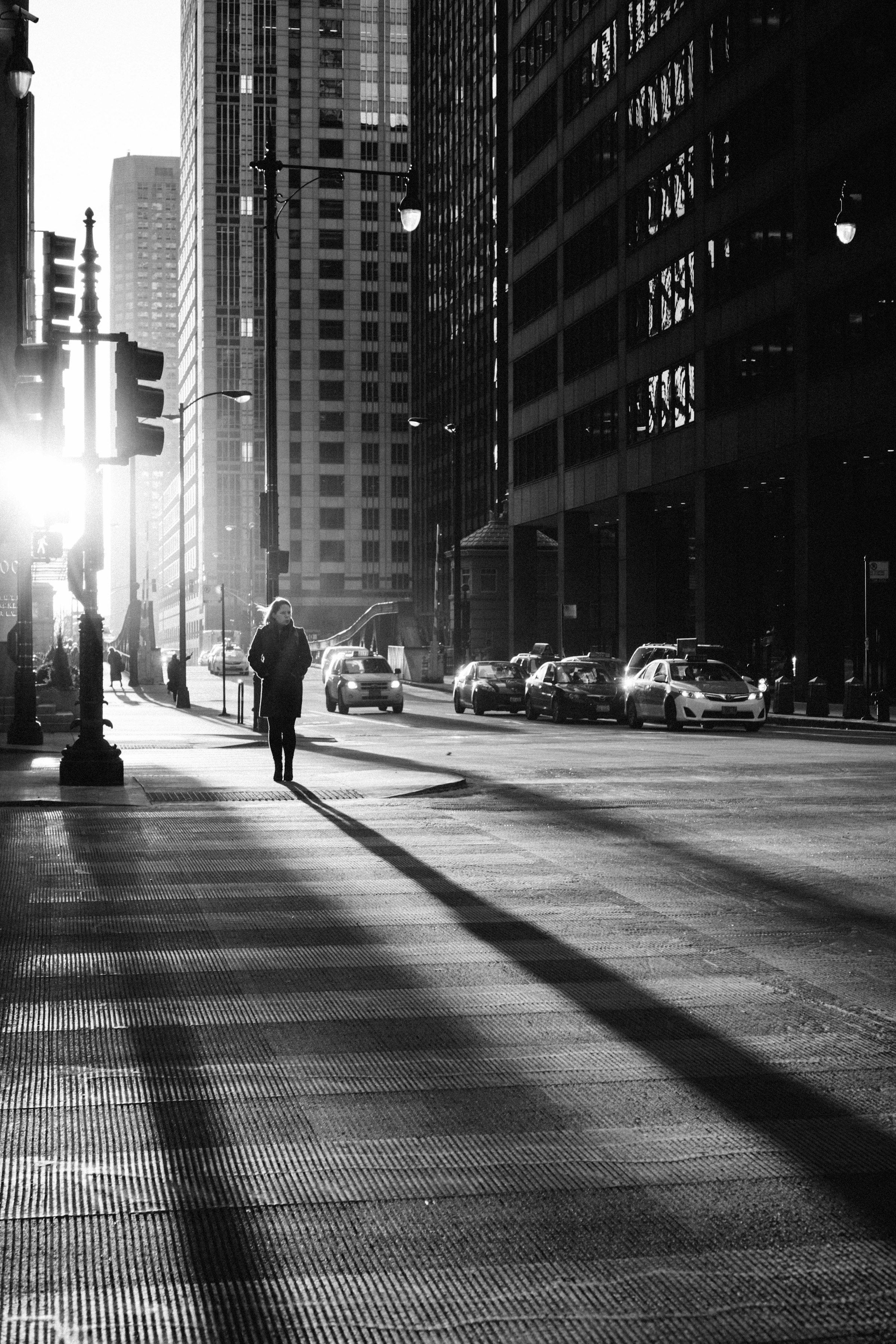 Schwarzweißfoto einer Straßenschlucht im Gegenlicht, Passanten werfen lange Schatten